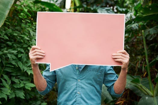 Individual in a blue shirt holds pink speech bubble in a green, leafy garden setting.